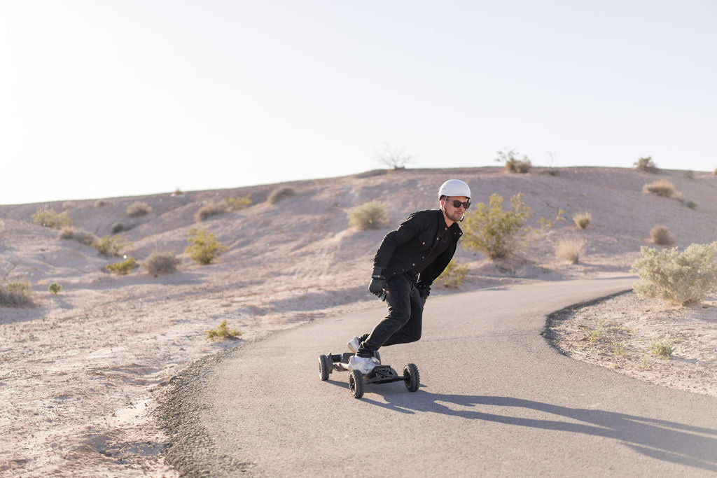 Rider on an ONSRA electric skateboard on a winding road in dry hills